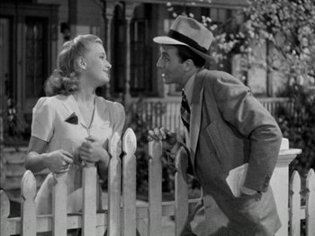 Movie still from “Four Daughters” (1938), directed by Michael Curtiz – A man and a woman standing next to each other near a fence; Medium shot, High angle