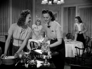 Movie still from “Four Daughters” (1938), directed by Michael Curtiz – A group of women standing around a table with food on it; Medium shot, Low angle