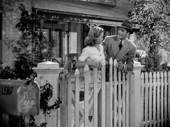 Movie still from “Four Daughters” (1938), directed by Michael Curtiz – A man and a woman standing in front of a white picket fence; Wide shot, Low angle