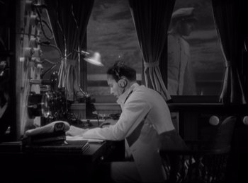 Movie still from “Four Frightened People” (1934), directed by Cecil B. DeMille – A man sitting at a desk in front of a laptop; Medium shot, High angle