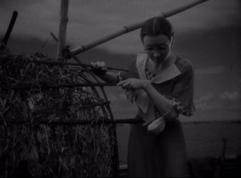 Movie still from “Four Frightened People” (1934), directed by Cecil B. DeMille – A woman standing in front of a basket with leaves; Medium shot, High angle