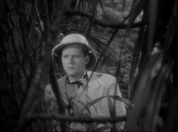 Movie still from “Four Frightened People” (1934), directed by Cecil B. DeMille – A black and white photo of a man in a suit and hat; Medium shot, High angle