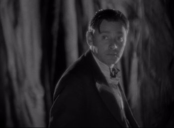 Movie still from “Four Frightened People” (1934), directed by Cecil B. DeMille – A black and white photo of a man in a suit and bow tie; Close Up shot, Low angle