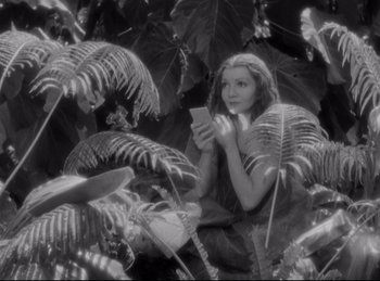 Movie still from “Four Frightened People” (1934), directed by Cecil B. DeMille – A woman sitting in a tree looking at her cell phone; Medium shot, High angle