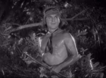 Movie still from “Four Frightened People” (1934), directed by Cecil B. DeMille – A man in a tie and a hat is holding an arrow in the woods; Medium shot, Low angle