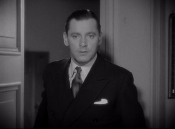 Movie still from “Four Frightened People” (1934), directed by Cecil B. DeMille – A man wearing a suit and tie standing in a room; Close Up shot, Low angle