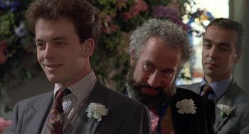Movie still from “Four Weddings and a Funeral” (1994), directed by Mike Newell – A man with a beard and flowers in his suit; Close Up shot, Over the shoulder angle
