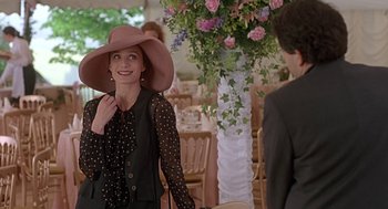 Movie still from “Four Weddings and a Funeral” (1994), directed by Mike Newell – A woman wearing a hat and a polka dot blouse; Medium shot, Over the shoulder angle