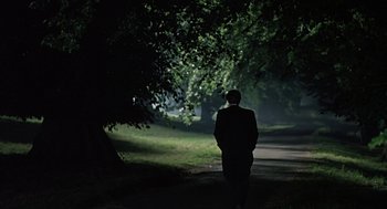 Movie still from “Four Weddings and a Funeral” (1994), directed by Mike Newell – A man in a suit is walking down a path in the dark; Wide shot, Low angle