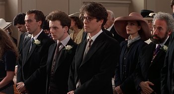 Movie still from “Four Weddings and a Funeral” (1994), directed by Mike Newell – A group of people in suits and ties standing in a room; Close Up shot, Low angle