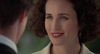 Movie still from “Four Weddings and a Funeral” (1994), directed by Mike Newell – A person with curly hair smiling; Close Up shot, Over the shoulder angle