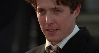 Movie still from “Four Weddings and a Funeral” (1994), directed by Mike Newell – A person wearing a suit and tie; Close Up shot, Low angle