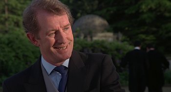 Movie still from “Four Weddings and a Funeral” (1994), directed by Mike Newell – A person wearing a suit and tie; Close Up shot, Over the shoulder angle