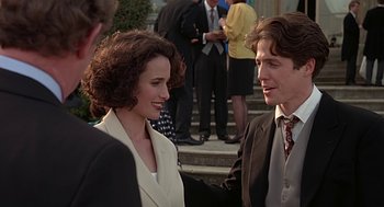 Movie still from “Four Weddings and a Funeral” (1994), directed by Mike Newell – A man and a woman shaking hands in front of a crowd; Medium shot, Over the shoulder angle