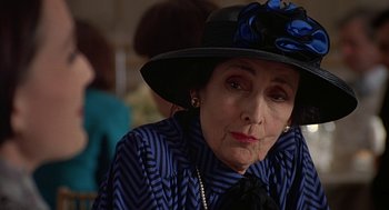 Movie still from “Four Weddings and a Funeral” (1994), directed by Mike Newell – An older woman wearing a blue striped shirt and a black hat; Close Up shot, Over the shoulder angle