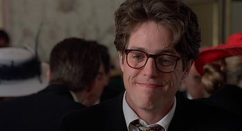 Movie still from “Four Weddings and a Funeral” (1994), directed by Mike Newell – A person wearing glasses and a suit; Close Up shot, Over the shoulder angle