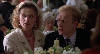 Movie still from “Four Weddings and a Funeral” (1994), directed by Mike Newell – A man and a woman sitting next to each other in front of flowers; Close Up shot, Over the shoulder angle