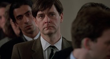 Movie still from “Four Weddings and a Funeral” (1994), directed by Mike Newell – A person wearing a suit and tie; Close Up shot, Over the shoulder angle