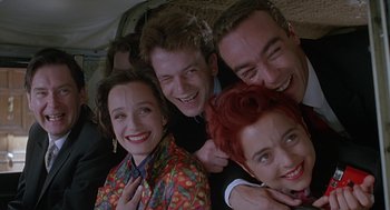 Movie still from “Four Weddings and a Funeral” (1994), directed by Mike Newell – A group of people posing for a picture together; Close Up shot, Low angle