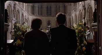 Movie still from “Four Weddings and a Funeral” (1994), directed by Mike Newell – A man and a woman standing next to each other in front of a building; Medium shot, Over the shoulder angle