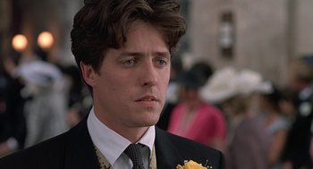 Movie still from “Four Weddings and a Funeral” (1994), directed by Mike Newell – A man in a suit and tie holding a yellow flower; Close Up shot, Over the shoulder angle