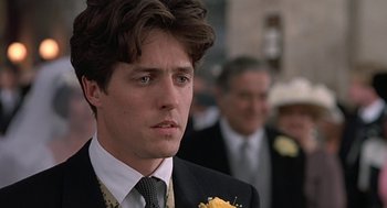 Movie still from “Four Weddings and a Funeral” (1994), directed by Mike Newell – A person wearing a suit and tie; Close Up shot, Over the shoulder angle