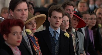 Movie still from “Four Weddings and a Funeral” (1994), directed by Mike Newell – A group of people standing next to each other wearing suits; Close Up shot, Over the shoulder angle
