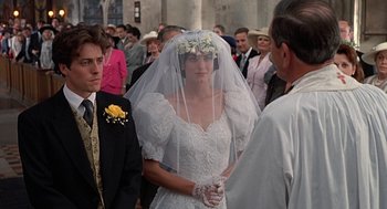 Movie still from “Four Weddings and a Funeral” (1994), directed by Mike Newell – A woman in a wedding dress and veil standing next to a crowd; Close Up shot, Over the shoulder angle