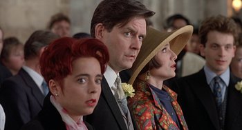 Movie still from “Four Weddings and a Funeral” (1994), directed by Mike Newell – A group of people standing next to each other in a room; Close Up shot, High angle