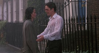 Movie still from “Four Weddings and a Funeral” (1994), directed by Mike Newell – A man and a woman standing next to each other near a fence; Medium shot, Over the shoulder angle