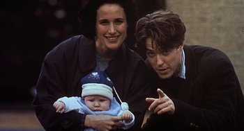 Movie still from “Four Weddings and a Funeral” (1994), directed by Mike Newell – A man and woman holding a baby and pointing; Medium shot, High angle