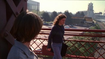 Movie still from “Foxfire” (1996), directed by Annette Haywood-Carter – A woman walking across a bridge holding a purse; Medium shot, Over the shoulder angle