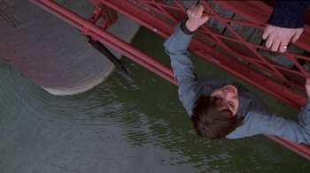 Movie still from “Foxfire” (1996), directed by Annette Haywood-Carter – A young boy hanging upside down from a red bridge; Wide shot, Overhead angle