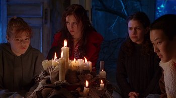 Movie still from “Foxfire” (1996), directed by Annette Haywood-Carter – A woman sitting in front of a bunch of lit candles; Medium shot, High angle