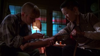 Movie still from “Foxfire” (1996), directed by Annette Haywood-Carter – A man is getting a tattoo on his forearm; Medium shot, Low angle