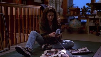 Movie still from “Foxfire” (1996), directed by Annette Haywood-Carter – A woman sitting on the ground looking at a phone; Medium shot, High angle