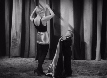 Movie still from “Freaks” (1932), directed by Tod Browning – A woman standing next to a man holding a curtain; Medium shot, Low angle
