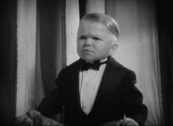 Movie still from “Freaks” (1932), directed by Tod Browning – A little boy wearing a suit and bow tie in front of a curtain; Medium shot, High angle