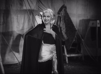 Movie still from “Freaks” (1932), directed by Tod Browning – A woman in a black and white photo holding a cape; Medium shot, High angle