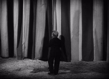 Movie still from “Freaks” (1932), directed by Tod Browning – A little boy standing in front of a stage curtain; Wide shot, Low angle