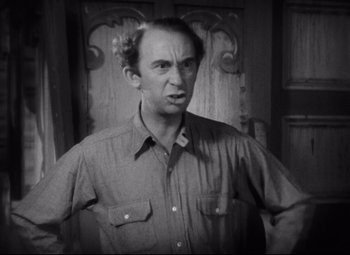 Movie still from “Freaks” (1932), directed by Tod Browning – An older man standing in front of a wooden door; Close Up shot, High angle