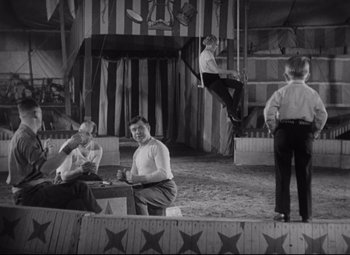 Movie still from “Freaks” (1932), directed by Tod Browning – A group of men sitting on top of a stage; Wide shot, Low angle