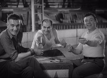 Movie still from “Freaks” (1932), directed by Tod Browning – A group of men sitting on top of a wooden table; Medium shot, Low angle