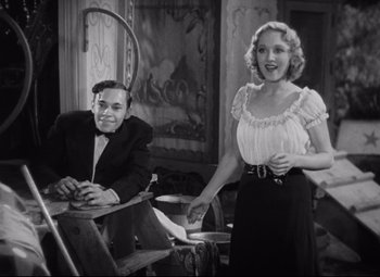 Movie still from “Freaks” (1932), directed by Tod Browning – A man and a woman standing next to each other in a room; Medium shot, Low angle