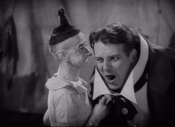 Movie still from “Freaks” (1932), directed by Tod Browning – A man is pulling on a man's neck tie; Medium shot, Low angle