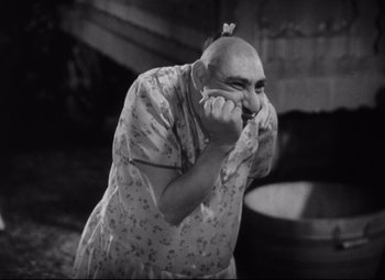 Movie still from “Freaks” (1932), directed by Tod Browning – An older man with a shaved head is holding his hands to his mouth; Medium shot, High angle