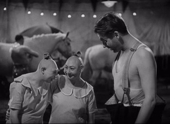 Movie still from “Freaks” (1932), directed by Tod Browning – A man and two women are standing in front of a horse; Medium shot, Low angle