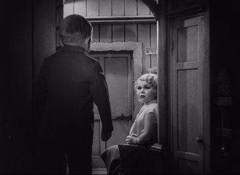 Movie still from “Freaks” (1932), directed by Tod Browning – A little girl sitting on a chair next to a man; Medium shot, High angle