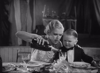 Movie still from “Freaks” (1932), directed by Tod Browning – A woman and a child at a table with a bottle of wine; Medium shot, High angle