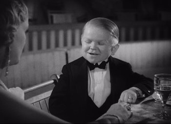 Movie still from “Freaks” (1932), directed by Tod Browning – A young boy in a tuxedo sitting at a table; Medium shot, High angle